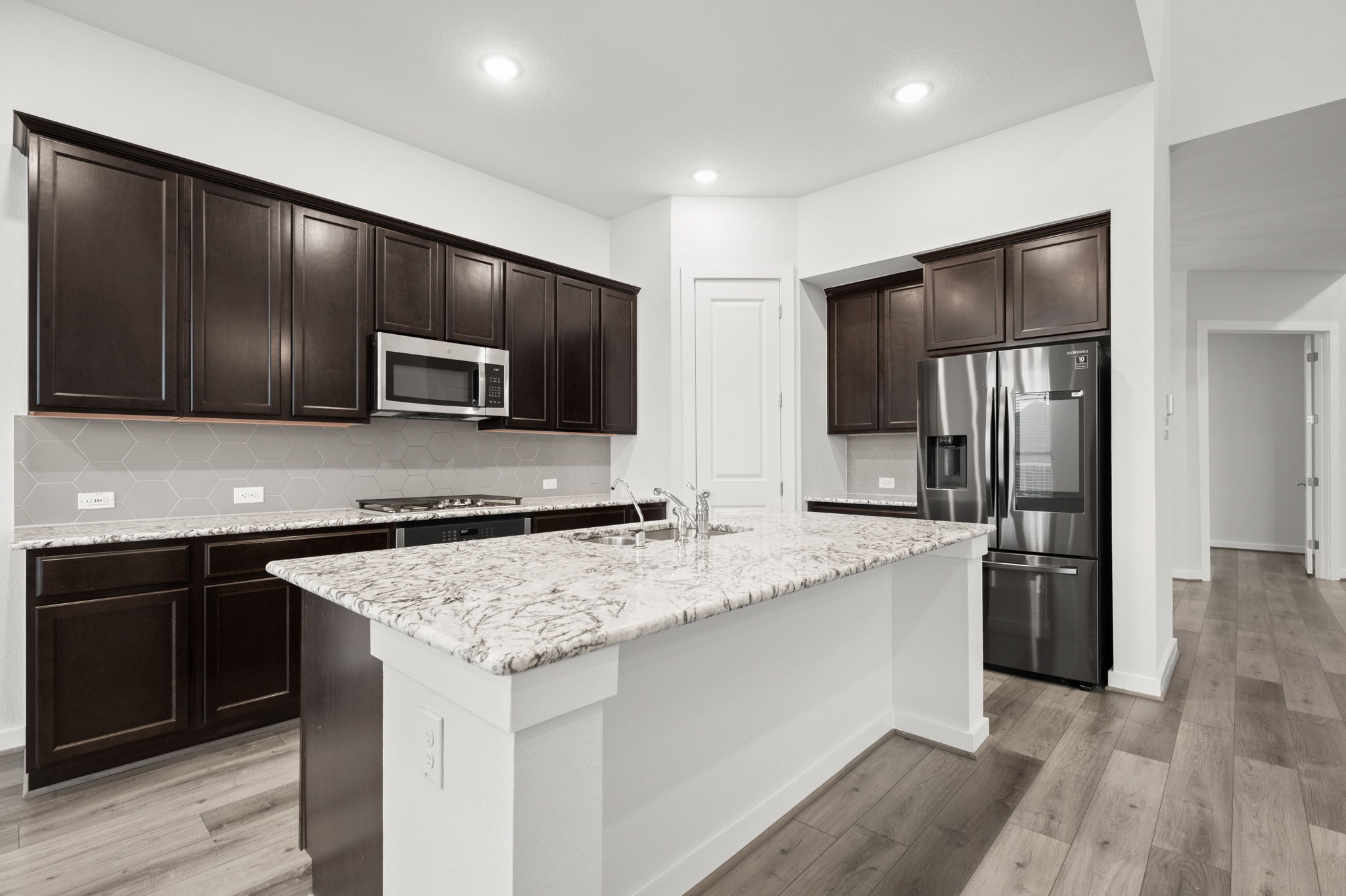 841 Spinnaker Loop Kyle, TX 78640 - Photo 16 of 40 Kitchen with dark brown cabinetry, stainless steel appliances, light stone counters, tasteful backsplash, and a center island with sink