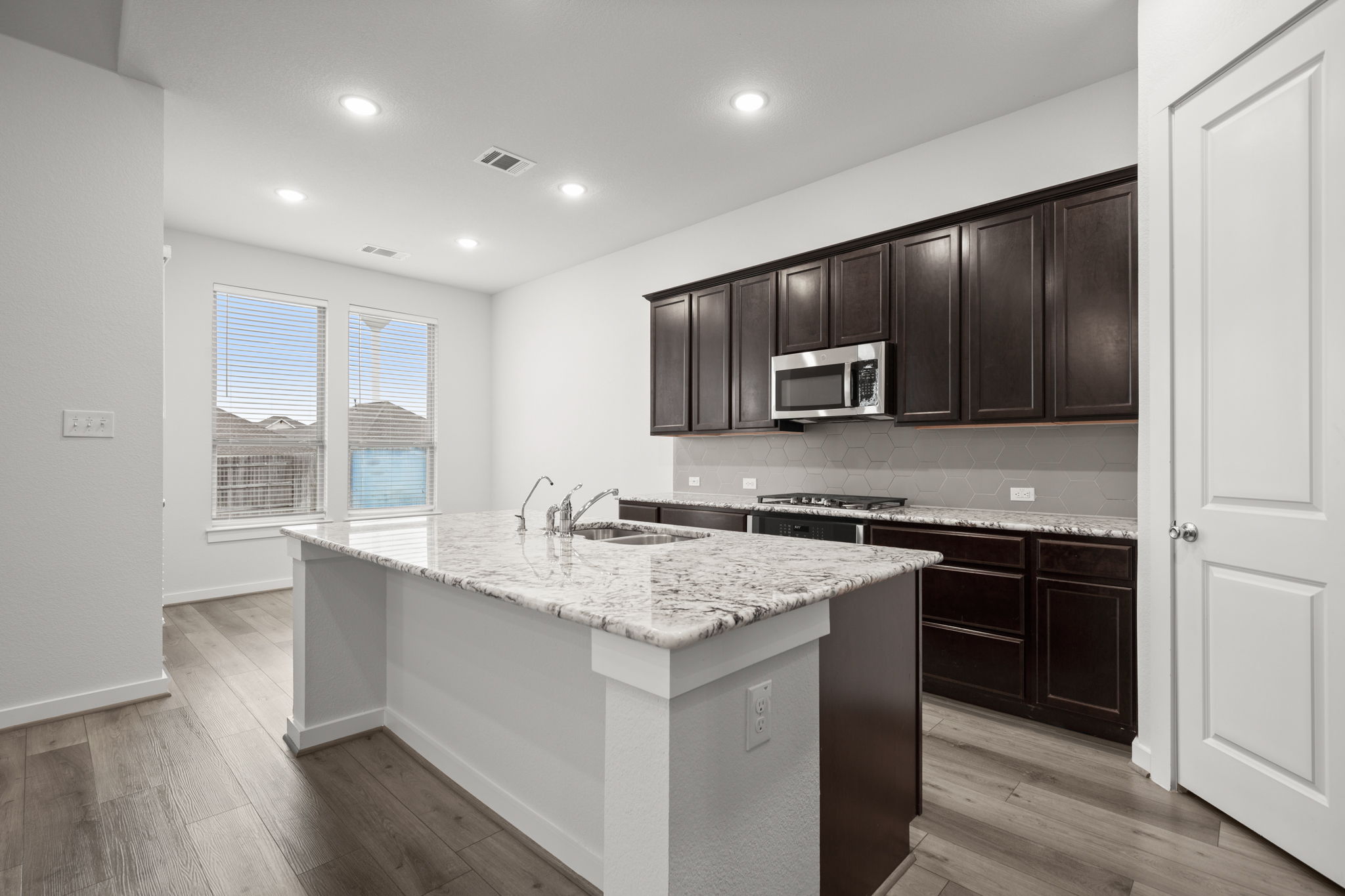 841 Spinnaker Loop Kyle, TX 78640 - Photo 18 of 40 Kitchen featuring light stone countertops, an island with sink, dark brown cabinetry, tasteful backsplash, and light wood finished floors
