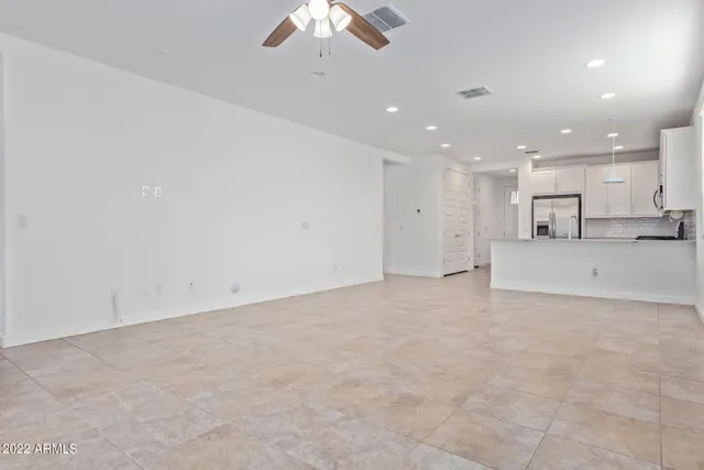 an empty room with kitchen view and a chandelier fan