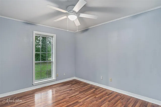 an empty room with wooden floor chandelier and windows