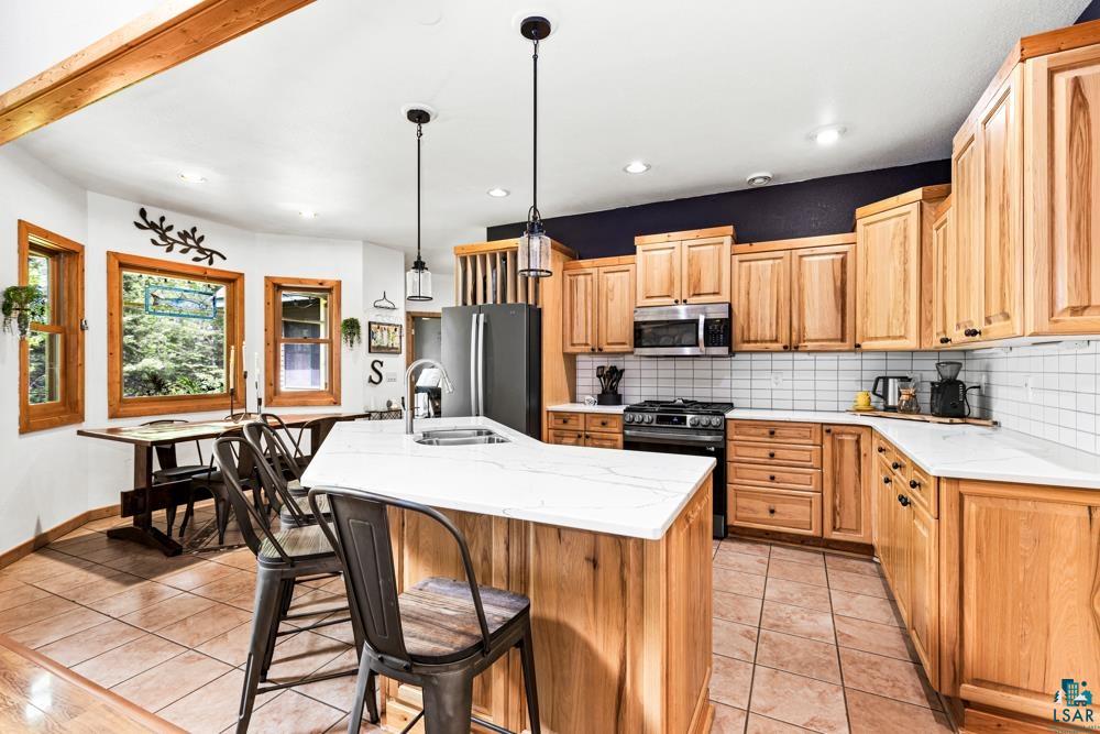 4471 South Rockmont Road South Range, WI 54874 - Photo 11 of 48 Kitchen featuring a center island with sink, black appliances, backsplash, pendant lighting, and light tile floors