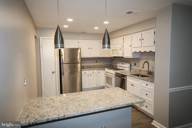 a kitchen with granite countertop a refrigerator oven a sink and white cabinets