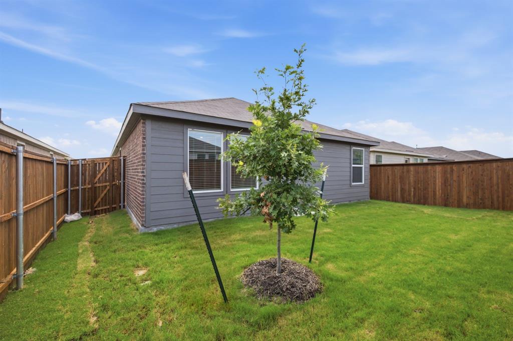 2128 Doc Holliday Road Joshua, TX 76058 - Photo 26 of 28 Expansive backyard featuring a manicured lawn, established privacy fencing, a young tree, and a brick and siding exterior