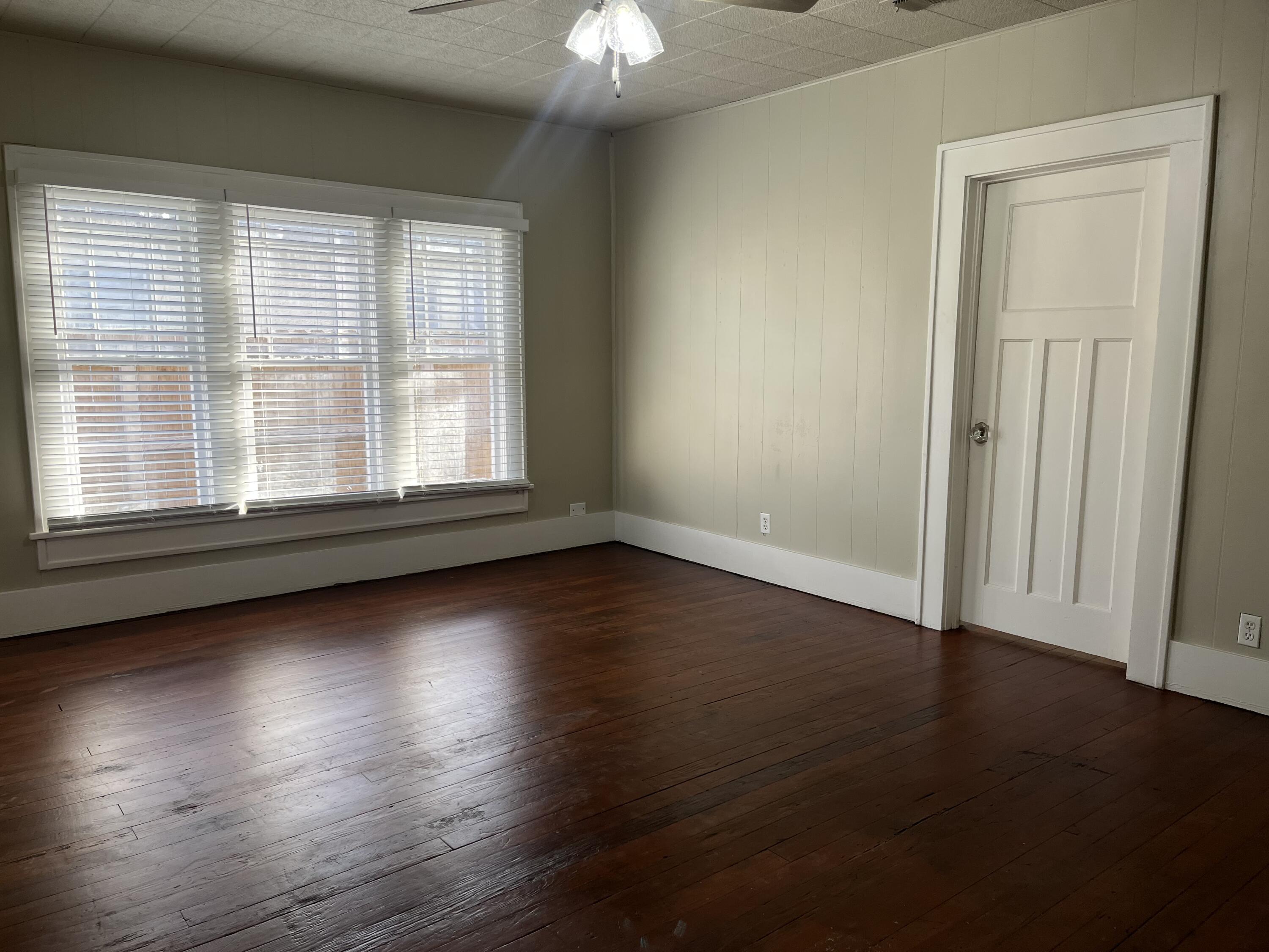 605 South 10th Street Slaton, TX 79364 - Photo 2 of 19 an empty room with wooden floor and windows