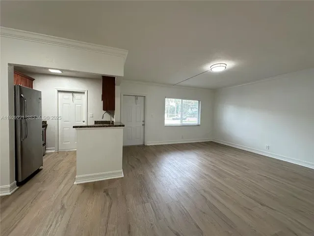 a view of a kitchen and an empty room with wooden floor and a kitchen