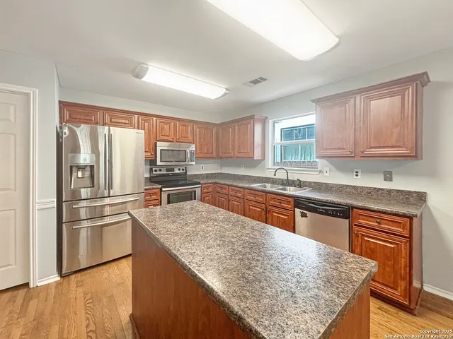 a kitchen with stainless steel appliances granite countertop a refrigerator a sink dishwasher a stove with wooden cabinets and floor