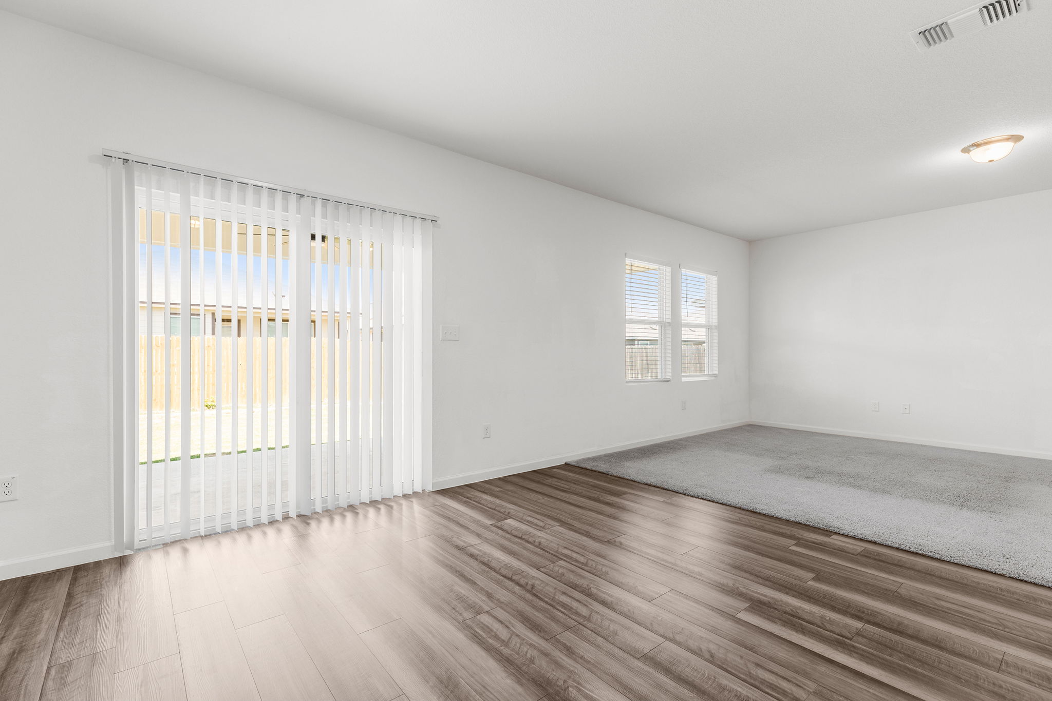 409 Line Of Fire Way Jarrell, TX 76537 - Photo 4 of 30 Open-concept living space featuring wood-finish flooring, light gray carpeting, recessed lighting, and a sliding glass door with vertical blinds leading to the backyard.