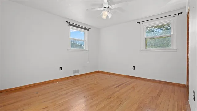 an empty room with wooden floor and ceiling fan