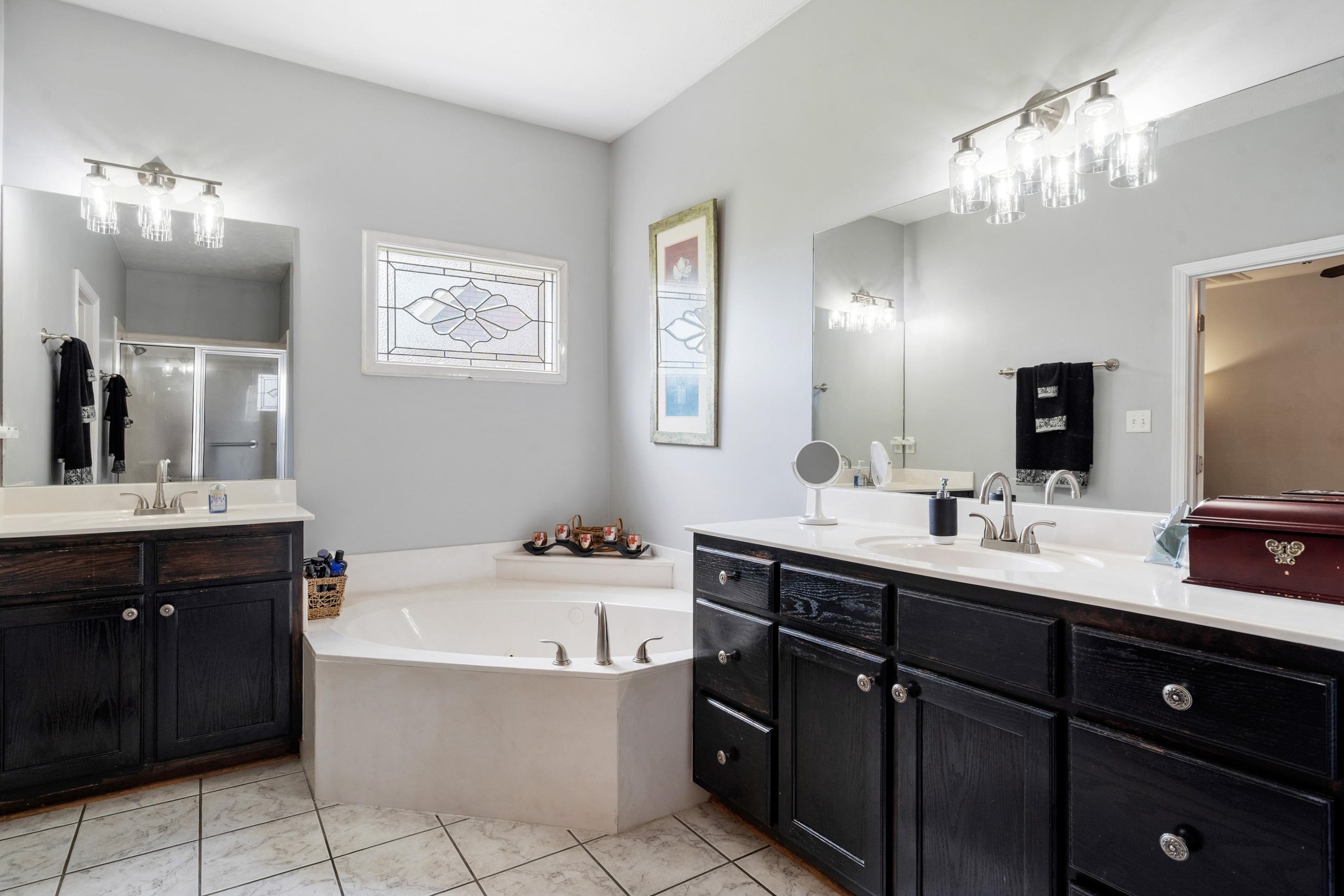 7757 Brunswick Road Millington, TN 38053 - Photo 12 of 40 Soaking tub with a decorative privacy window, dual vanities featuring dark cabinetry, and tile flooring