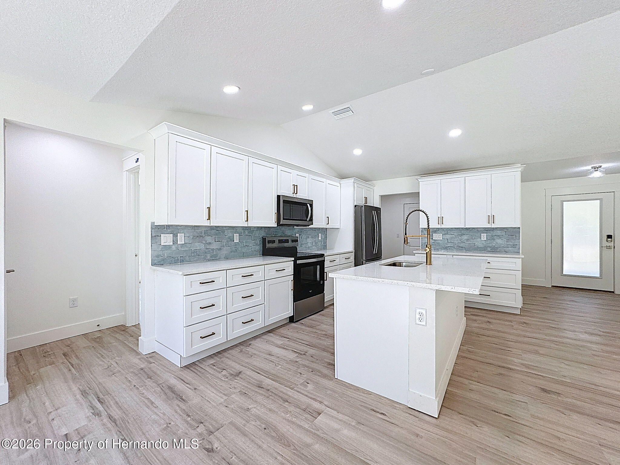 8988 Waterbird Way Weeki Wachee, FL 34613 - Photo 14 of 42 a large kitchen with stainless steel appliances granite countertop a stove top oven a sink a refrigerator white cabinets and couches with wooden floor