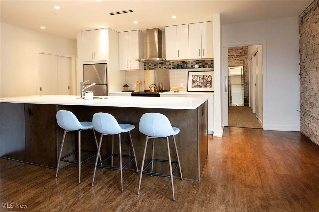 725 Johnson Court, Unit 220 Cleveland, OH 44113 - Photo 9 of 25 Kitchen featuring a breakfast bar, wall chimney exhaust hood, white cabinetry, and dark wood-style floors.