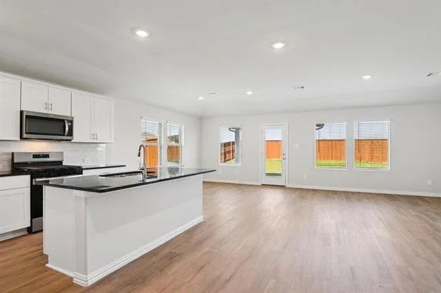 a view of an empty room with wooden floor and a kitchen