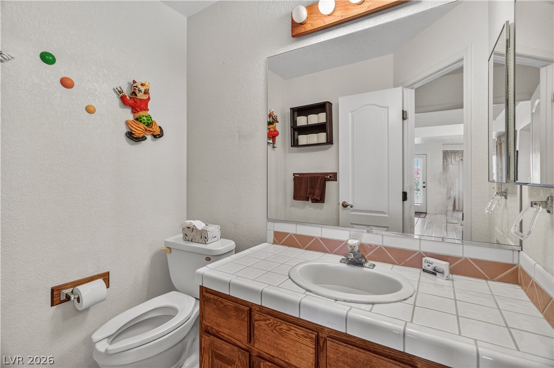 2055 Cholla Way Laughlin, NV 89029 - Photo 42 of 87 Functional vanity and toilet setup in the half bathroom, featuring tiled counters and warm wood cabinetry, provide everyday convenience.