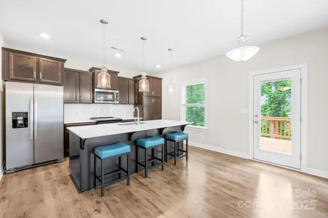 a kitchen with stainless steel appliances granite countertop a stove a refrigerator a sink a dining table and chairs with wooden floor