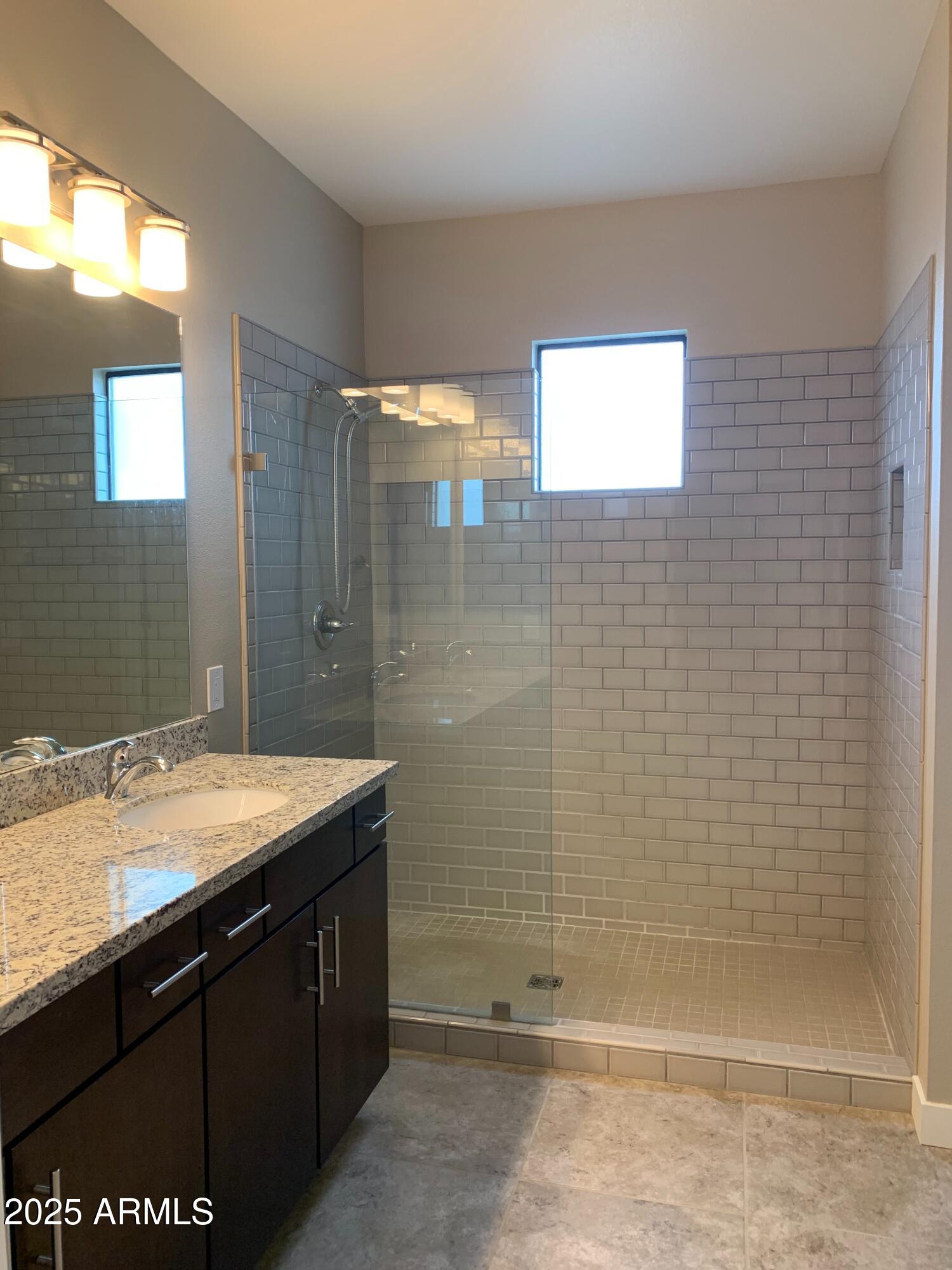 2511 West Queen Creek Road, Unit 326 Chandler, AZ 85248 - Photo 20 of 32 a bathroom with a granite countertop sink a shower and a mirror