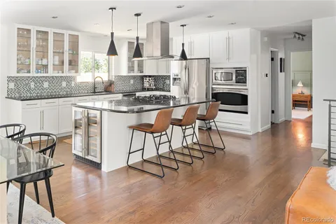 a kitchen with stainless steel appliances granite countertop a stove a refrigerator a sink a dining table and chairs with wooden floor