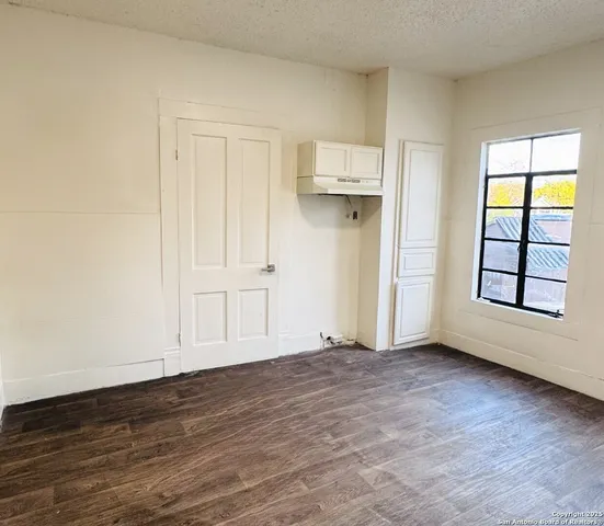 an empty room with wooden floor cabinet and windows
