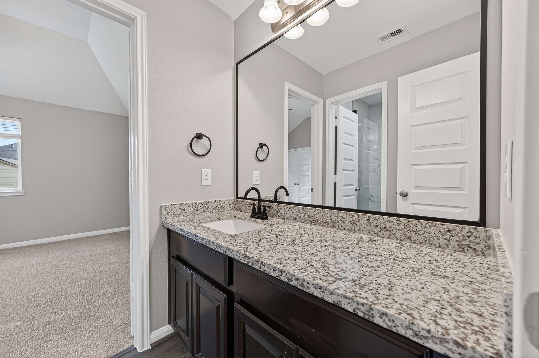 7003 Bristol Memorial Drive Spring, TX 77379 - Photo 38 of 40 Jack-and-Jill style bathroom positioned between two secondary bedrooms in this Spring TX 77379 home, offering dual access for added functionality. Features include granite countertops, undermount sink, framed mirror, and dark cabinetry for a clean, updated look. The connected layout provides convenience while maintaining separation from the main living areas. Designed for efficiency and everyday ease, this well-appointed bath enhances the smart upper-level floorplan in this move-in ready home