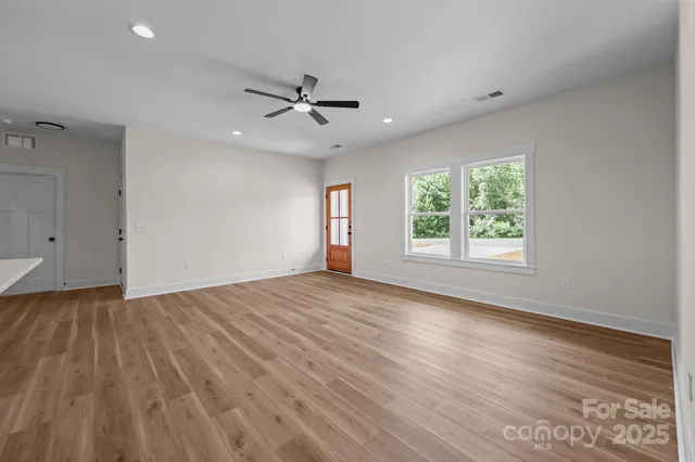 an empty room with wooden floor fan and windows