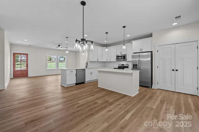 a kitchen with stainless steel appliances granite countertop a refrigerator a oven a sink dishwasher and white cabinets with wooden floor