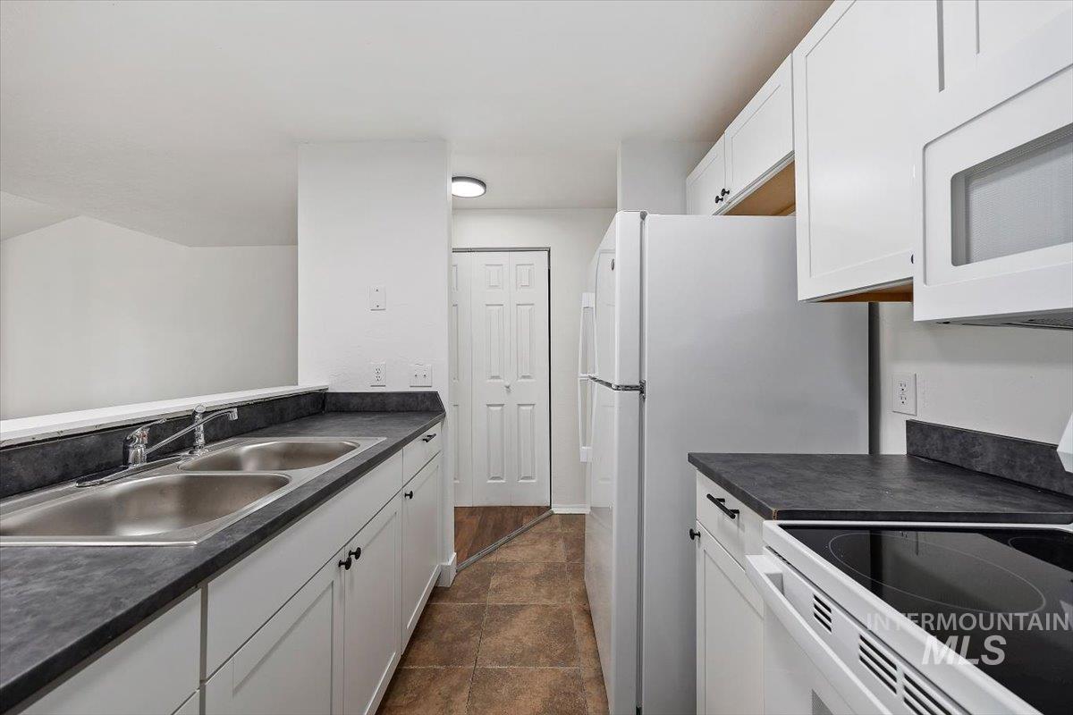259 Pheasant Road, Unit 84 Twin Falls, ID 83301 - Photo 11 of 25 Galley kitchen featuring white cabinetry, dark countertops, a double basin stainless steel sink, and a white electric range with a smooth cooktop