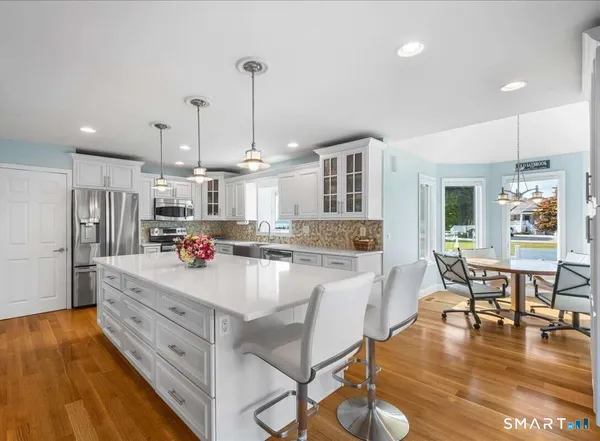 a room with stainless steel appliances kitchen island granite countertop a table chairs stove and a wooden floor