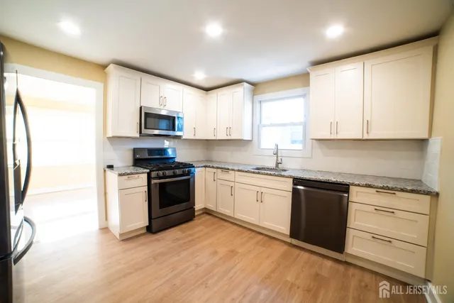 a kitchen with granite countertop a stove top oven a sink dishwasher and a refrigerator with wooden floor