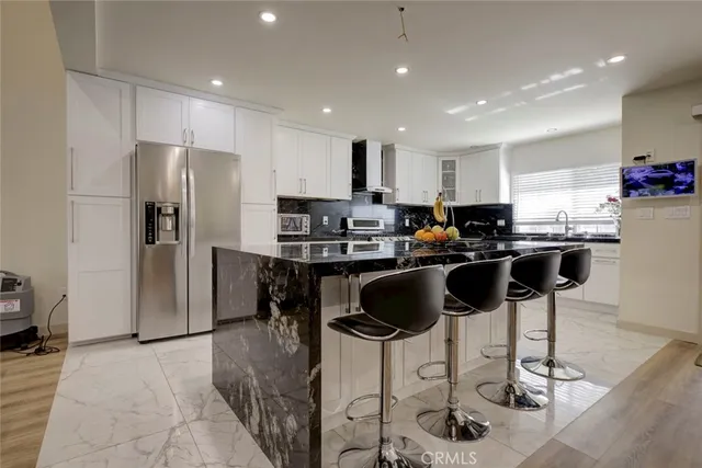 a kitchen with stainless steel appliances kitchen island granite countertop a refrigerator and a stove top oven with white cabinets