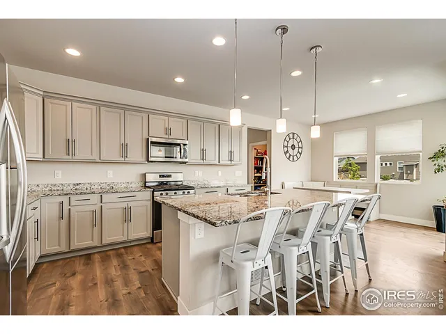 a kitchen with stainless steel appliances granite countertop a stove top oven a refrigerator a sink and a dining table with wooden floor