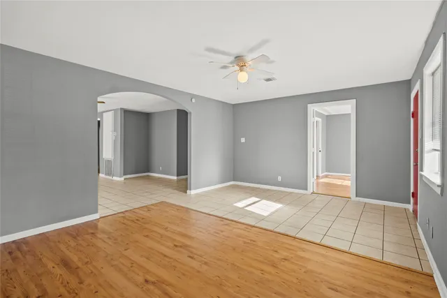 a view of an empty room with wooden floor and a chandelier fan