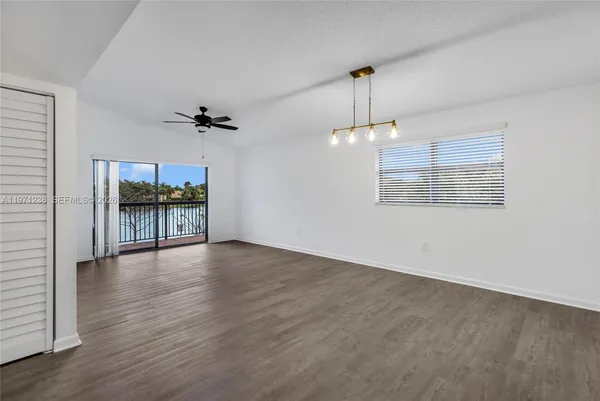 an empty room with wooden floor a chandelier fan and windows