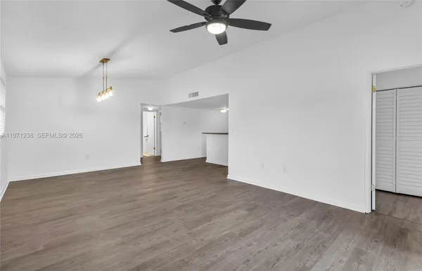 a view of an empty room with wooden floor and a ceiling fan