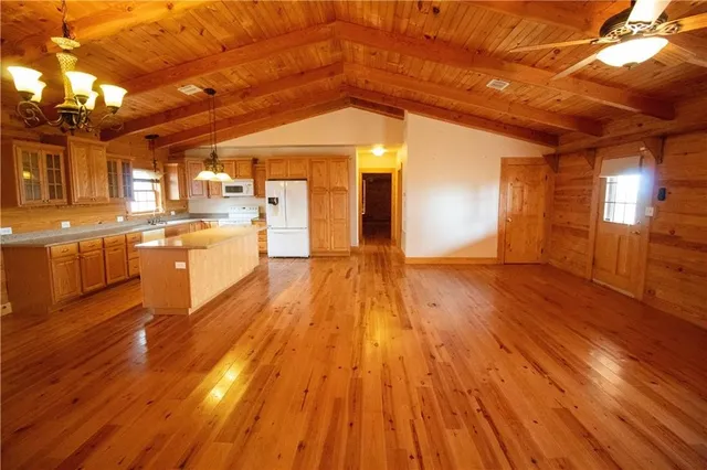 a view of an empty room with wooden floor and a kitchen