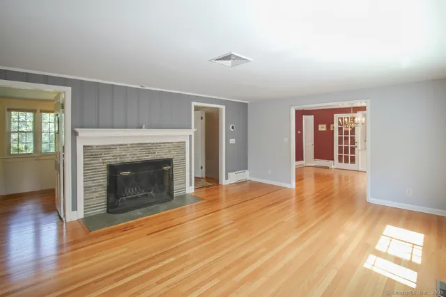 a view of an empty room with wooden floor fireplace and a window