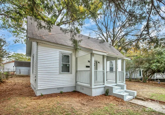 a view of a small house with a large tree and wooden fence