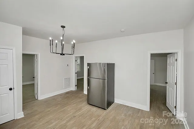 a an empty room with wooden floor kitchen view and a refrigerator