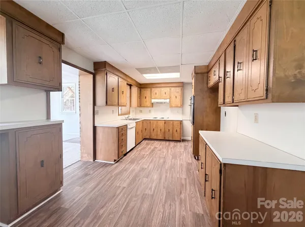 a kitchen with stainless steel appliances granite countertop a refrigerator a sink dishwasher a stove and white countertops with wooden floor
