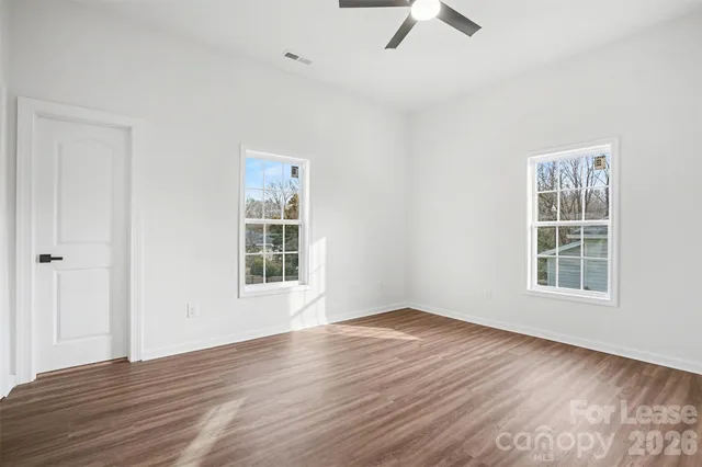 an empty room with wooden floor fan and windows