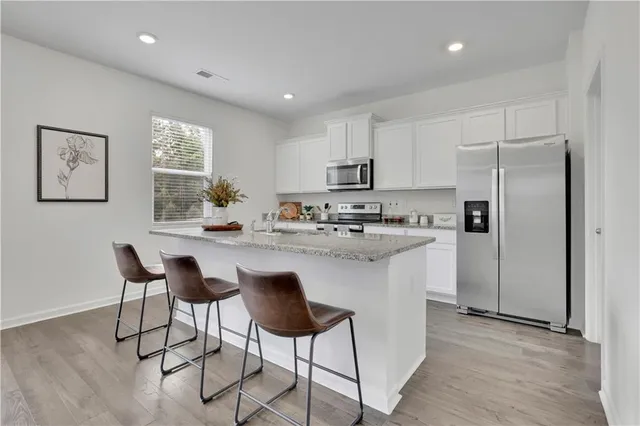 a kitchen with kitchen island granite countertop a refrigerator a stove a sink and white cabinets with wooden floor