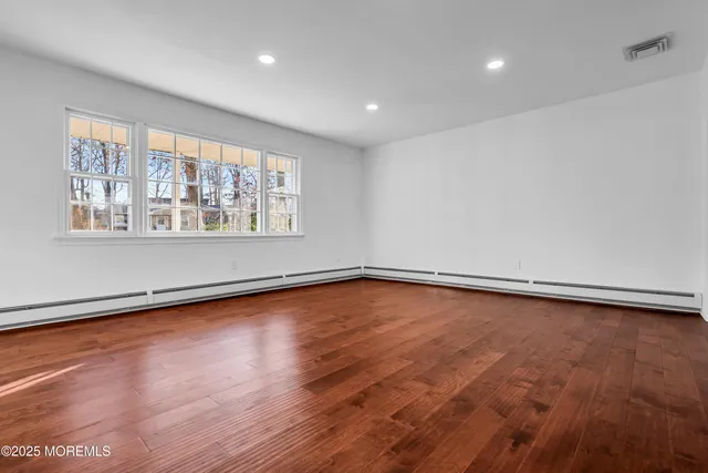 a view of empty room with wooden floor and kitchen view