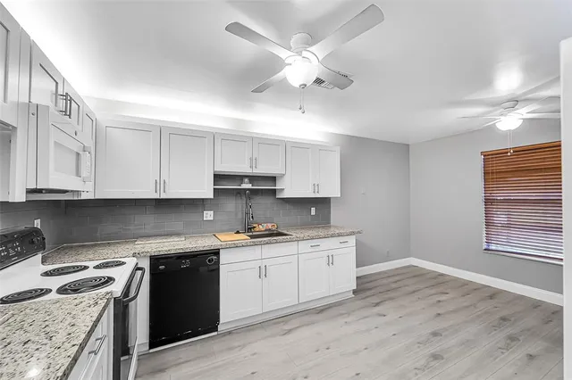 a kitchen with stainless steel appliances granite countertop a stove a sink dishwasher and white cabinets with wooden floor