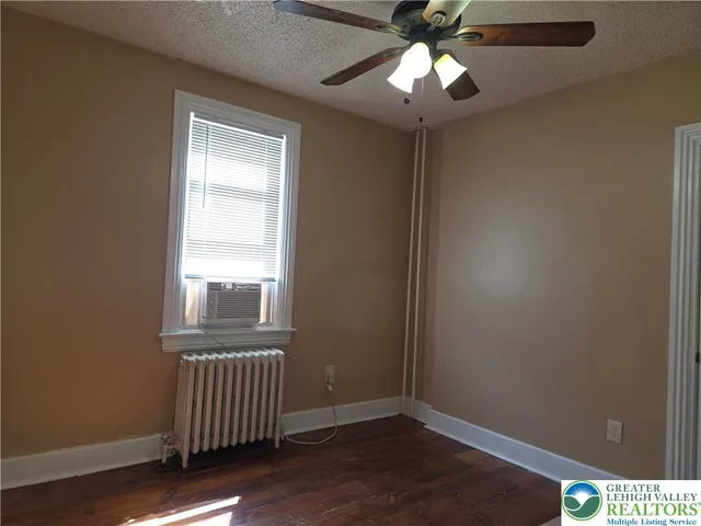 an empty room with wooden floor chandelier fan and windows