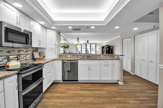 a kitchen with stainless steel appliances granite countertop a stove top oven a sink dishwasher and white cabinets with wooden floor