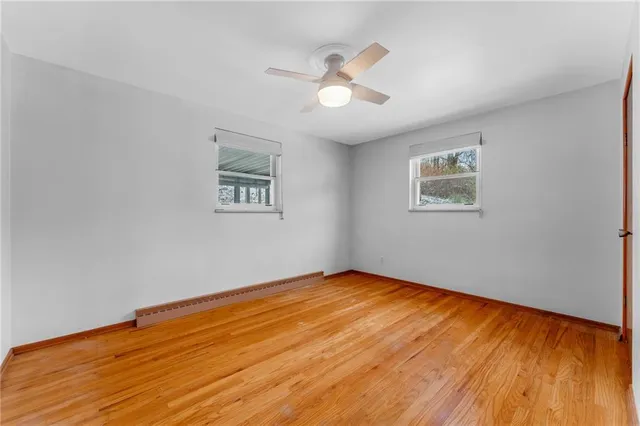 a view of an empty room with wooden floor and a ceiling fan