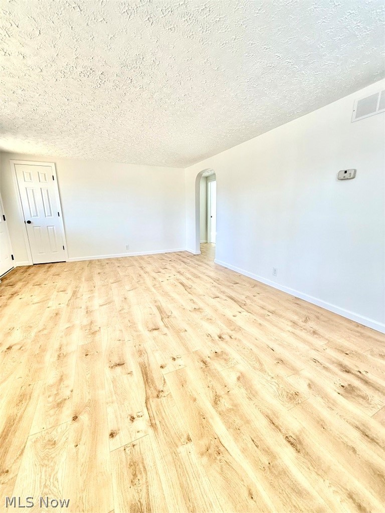 144 Aberdeen Road Steubenville, OH 43953 - Photo 6 of 34 Empty room featuring arched walkways, a textured ceiling, and light wood-type flooring