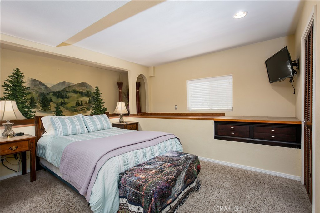 10960 Steinhoff Road Frazier Park, CA 93225 - Photo 41 of 46 The cozy 5th bedroom, conveniently located on the lower level. This comfortable space features soft carpeting, a unique custom-painted mountain landscape wall mural, a window offering natural light, and a long built-in dark wood dresser with extensive counter space and storage.