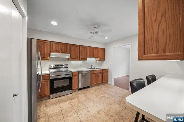 a kitchen with stainless steel appliances granite countertop a stove top oven a sink dishwasher and a refrigerator with wooden cabinets