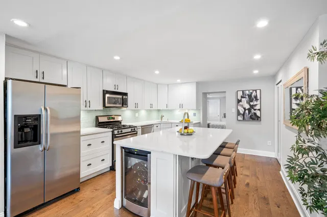 a kitchen with stainless steel appliances granite countertop a refrigerator a stove a sink a microwave a dining table and chairs with wooden floor