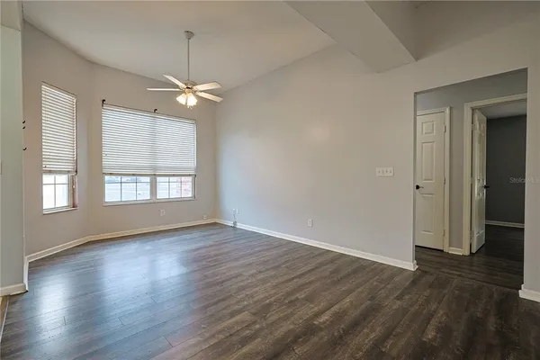 an empty room with wooden floor chandelier fan and windows
