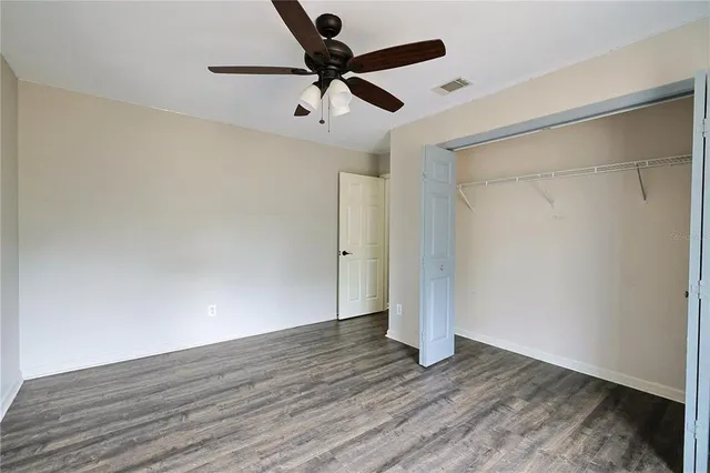an empty room with wooden floor ceiling fan and windows